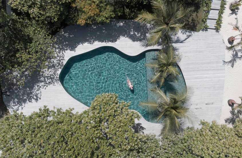 Em um dia ensolarado, vista aérea da área de lazer com piscina, deck de madeira e árvores ao redor