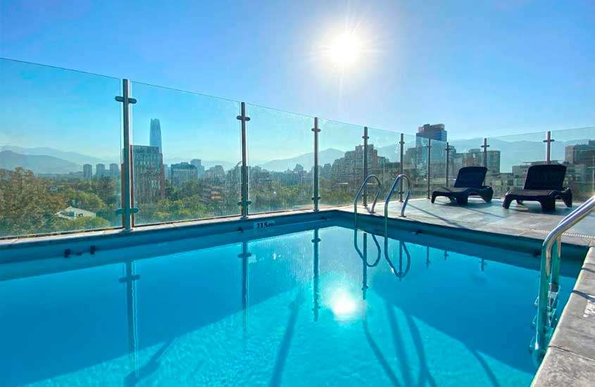 Em um dia de sol, área de lazer de um hotel em santiago do chile com piscina, espreguiçadeiras e paisagem da cidade