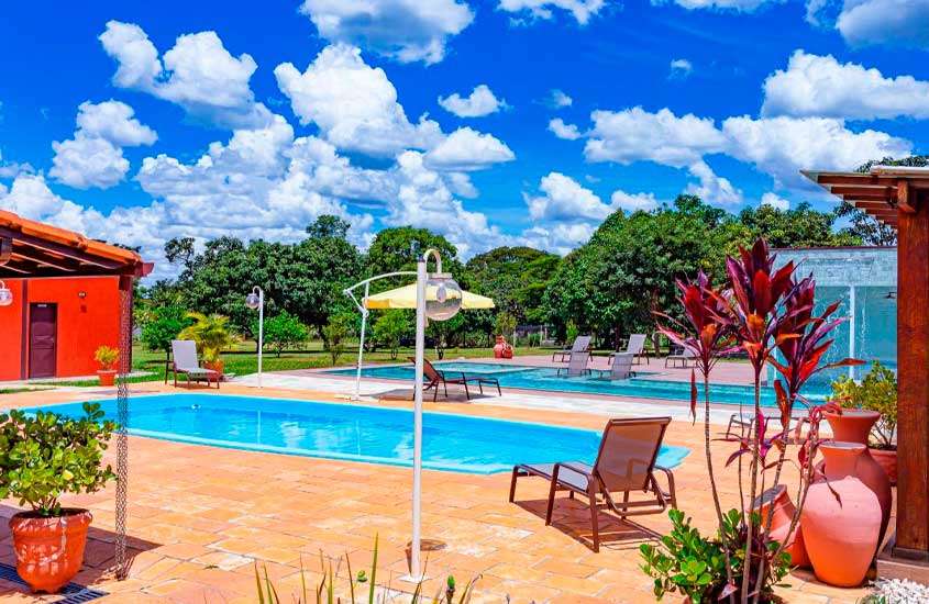 Em um dia de sol com nuvens, área de lazer de um dos lugares perto de Brasília para passar o feriado com piscinas, espreguiçadeiras, plantas e árvores ao redor