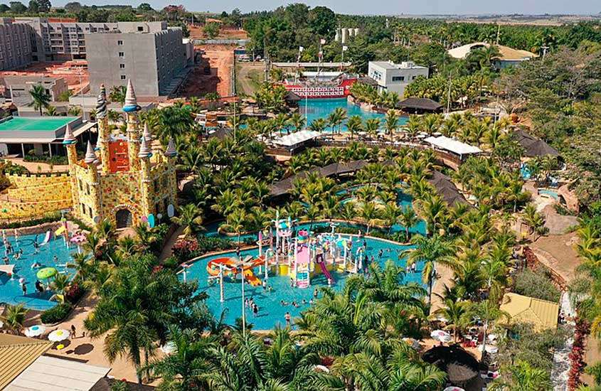 Em um dia de sol, vista aérea de um hotel de um dos lugares para fugir do carnaval com piscinas, brinquedos de água, castelo e árvores ao redor