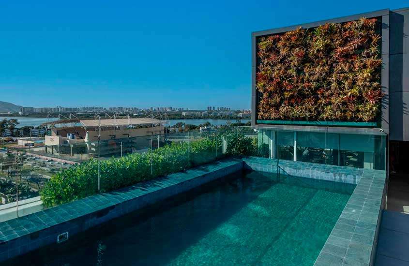 Em um dia de sol, área de lazer de um dos hotéis perto do rock in rio com piscina, área gramada e plantas decorativas