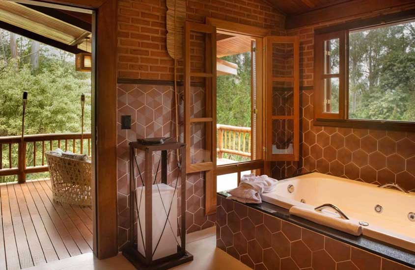 Banheiro e deck de madeira com banheira, toalhas, poltrona, janelas e portas grandes