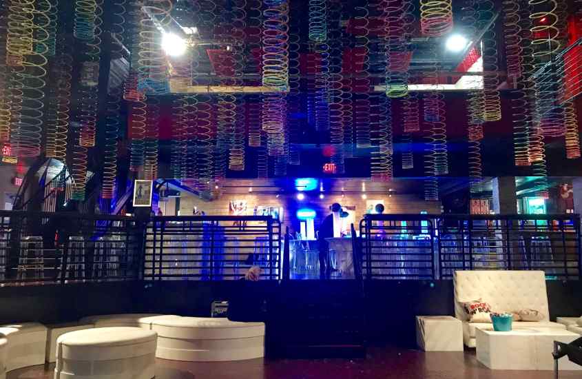 Interior do Revolution Live, com bar, luzes coloridas, mesas e cadeiras
