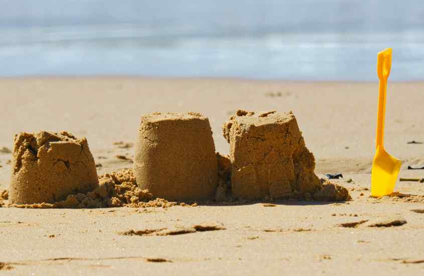 Em um dia de sol, castelinho de areia com pazinha e mar na frente