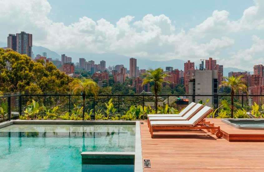 Durante um dia ensolarado, área de lazer de um dos melhores apartamentos em Medellín com piscina, espreguiçadeiras e paisagem da cidade