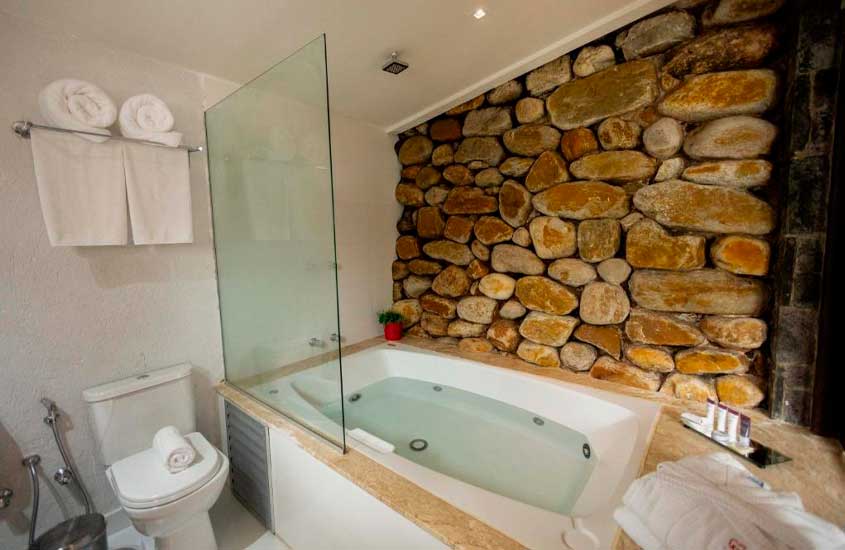 Banheiro de uma pousada com banheira, toalhas, parede de pedra e amenities