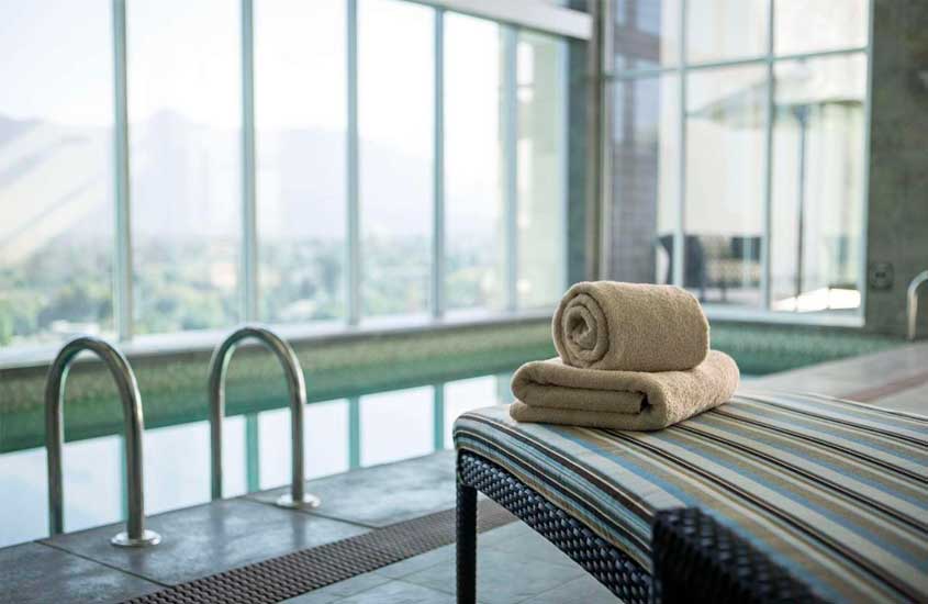Área de lazer coberta de um melhores hoteis em santiago do chile com piscina, espreguiçadeira, paisagem da cidade e toalhas