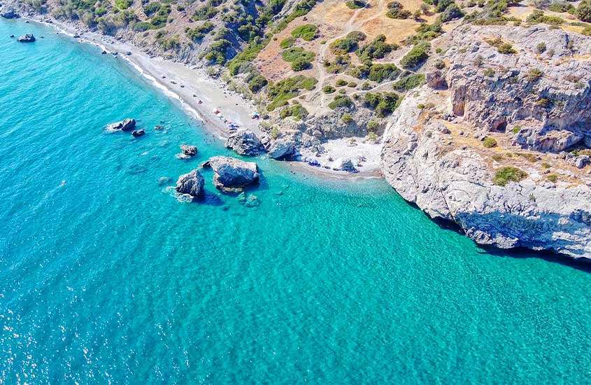 Vista aérea de uma das praias em Creta com pedras ao redor e árvores no meio