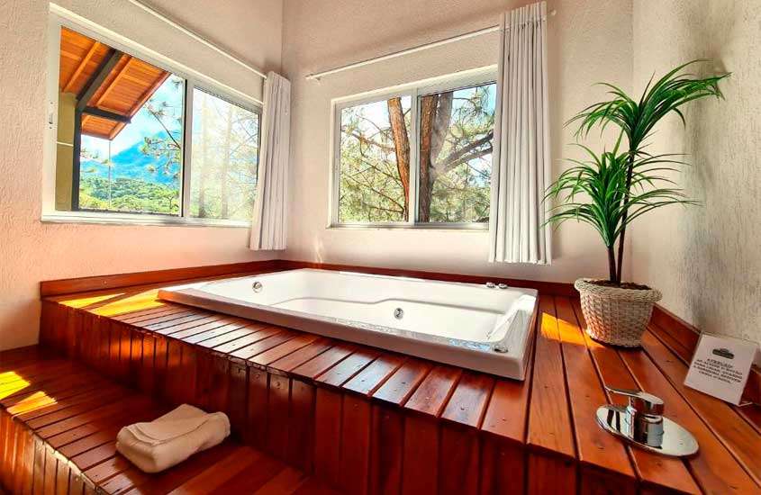 Área de banheira com deck de madeira de um dos hotéis românticos no rio de janeiro com toalha, vaso de planta e janelas acortinadas