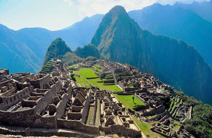 Em um dia de sol, visitar o Machu Picchu é um dos passeio mais famosos do que fazer em cusco com montanhas ao redor e ruinas no meio