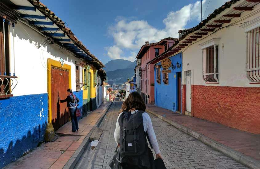 Em um dia de sol, viajante andando na rua com casas coloridas e montanhas no fundo