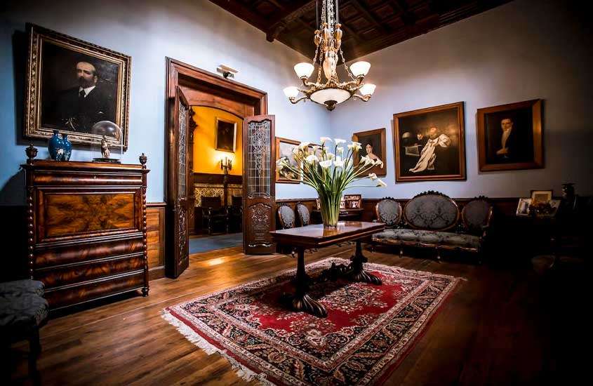 Interior de um ponto turístico de lima com mesa, sofás, tapete, flores decorativas, quadros e móveis de madeira