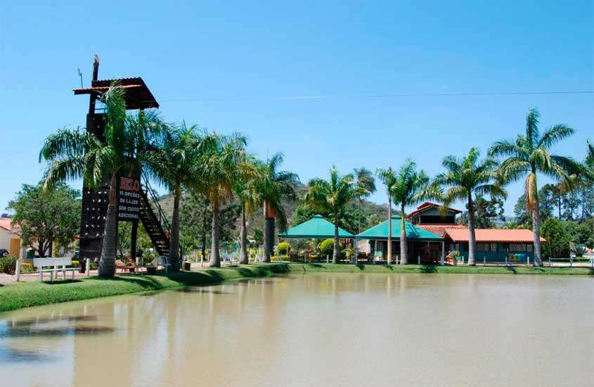 Em um dia de sol, lago de um hotel fazenda em socorro com árvores, bancos, acomodações e casinha de salva-vidas