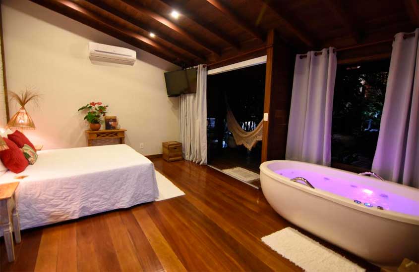 Quarto de um dos hotéis românticos no rio de janeiro com cama de casal, banheira, tapete, TV, varanda com rede e ar condicionado