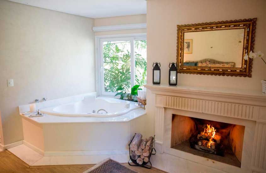 Área de banheira de um dos hotéis românticos no rio de janeiro com lareira ao lado espelho, tapete, toalhas e janela grande
