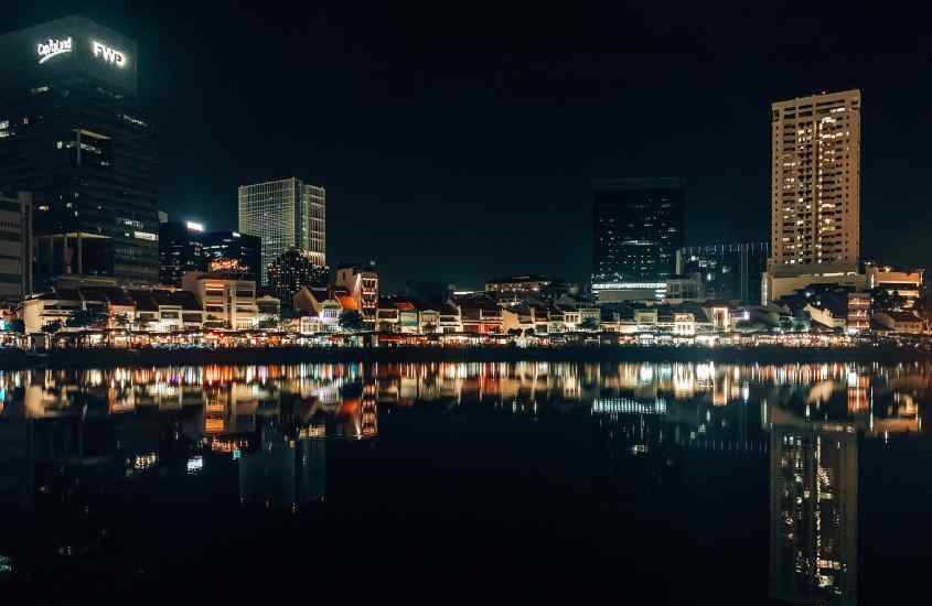 Durante a noite, paisagem de um bairro iluminado onde ficar em singapura refletida na água