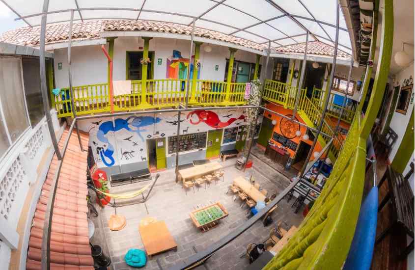 Vista aérea de área externa de um hostel em Cusco com mesas, cadeiras, redes, totó, sofás e pintura decorativas na parede