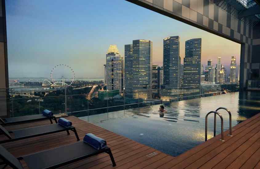 Final do dia, área de lazer de hotel em singapura com piscina, paisagem da cidade, espreguiçadeiras e deck de madeira