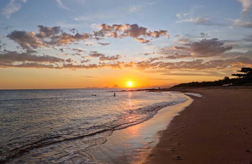Durante o pôr do sol, praia de Guarapari, um dos lugares para onde viajar no feriado de corpus christi com pessoas no mar e árvores ao redor