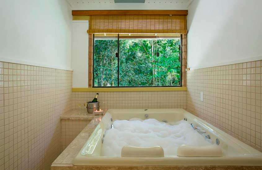 Área de banheira de espuma de um dos hotéis românticos no rio de janeiro com balde de champagne, velas e janela com paisagem da natureza