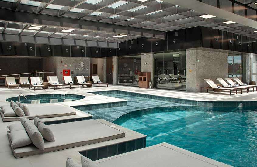 Área de lazer de um hotel com piscinas, espreguiçadeiras, camas e iluminação natural