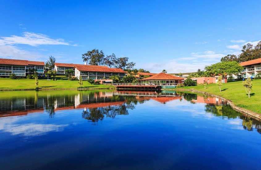 Em um dia de sol, lago de um dos hotéis fazenda em Pernambuco com árvores e parte gramada ao redor