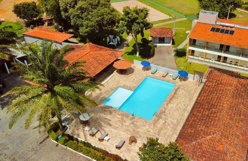 Em um dia de sol, vista aérea de um dos hotéis fazenda em Pernambuco com piscina, espreguiçadeiras, guarda-sóis e árvores ao redor