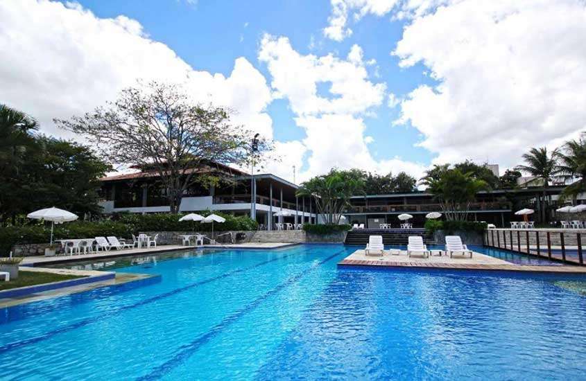 Em um dia de sol com nuvens, área de lazer de um dos hotéis fazenda em Pernambuco, com piscina, espreguiçadeiras, guarda-sóis e árvores ao redor