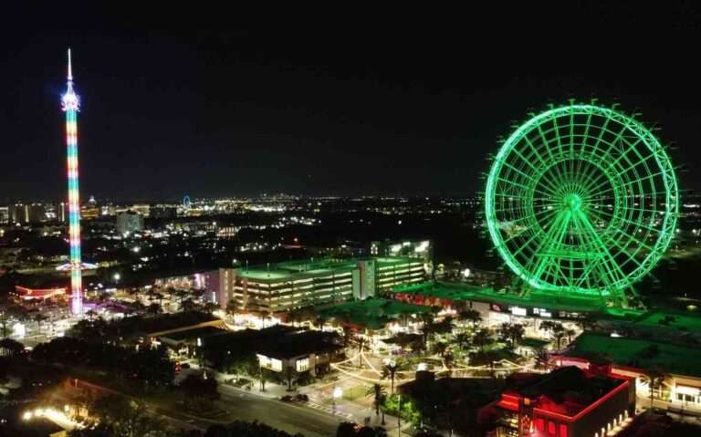 Durante a noite, vista aérea de Orlando com roda gigante iluminada, brinquedo com luzes coloridas, árvores e prédios ao redor