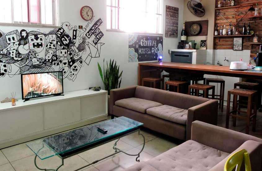 Sala de hotel perto do sambódromo no rio de janeiro com sofás, mesas, bancos, TV, paredes decoradas e ventilador