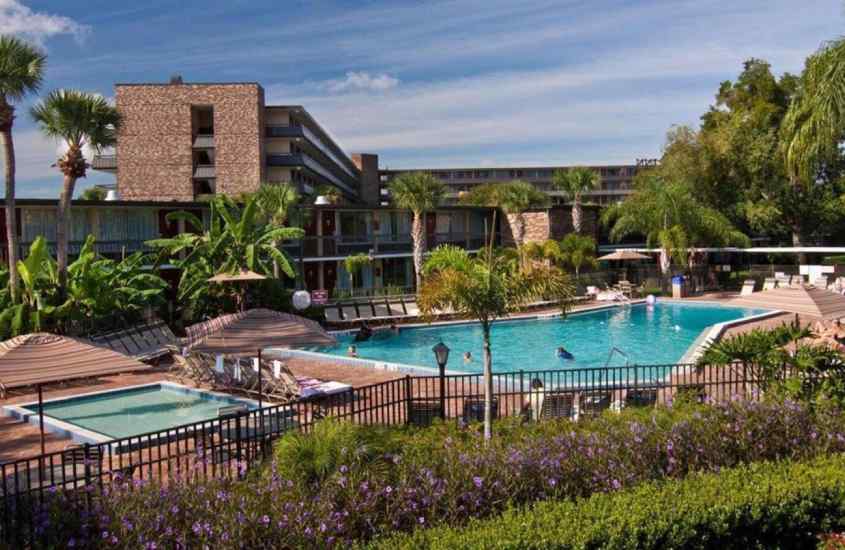 Em um dia de sol, área de lazer de um dos hotéis em orlando na international drive com piscinas, guarda-sóis, espreguiçadeiras, árvores e plantas ao redor