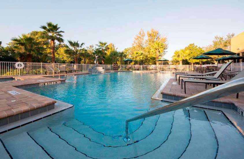 Durante o entardecer, área de lazer de um dos hotéis baratos em Orlando perto da disney com piscina, espreguiçadeiras, guarda-sóis e árvores ao redor