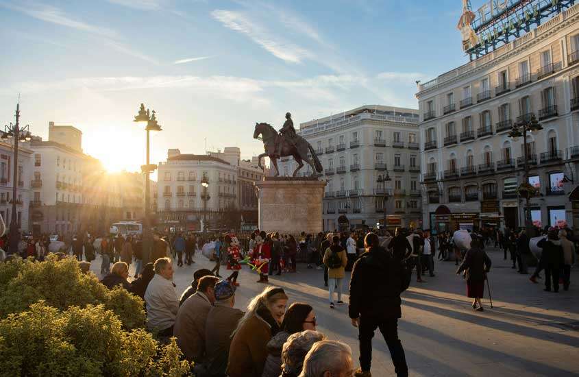 Durante o pôr do sol, área do centro da cidade de madrid com pessoas, escultura no meio e prédios ao redor
