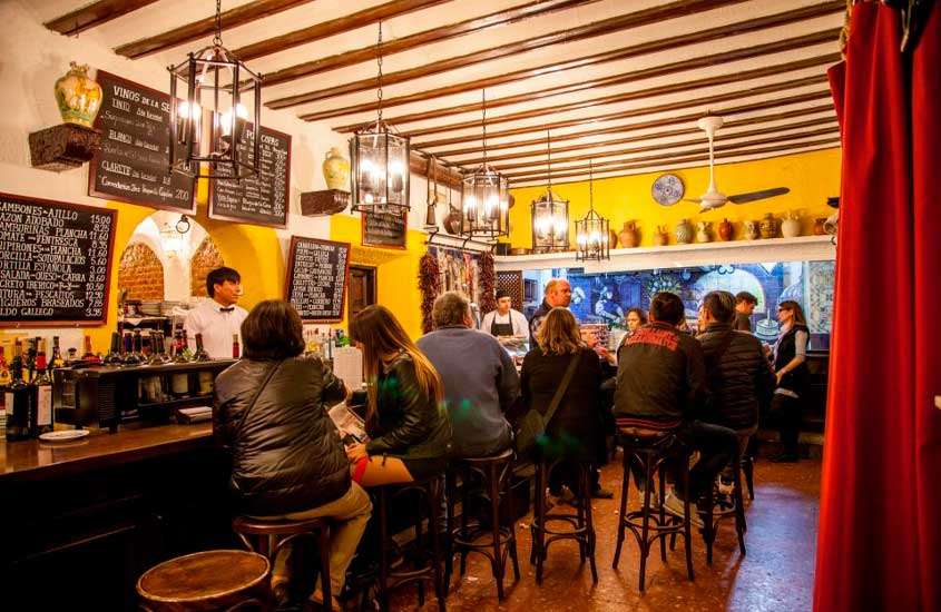 Um dos bares da cidade de madrid com pessoas dentro, quadros negros, bebidas e decorações ao redor