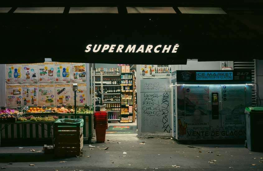 Fachada de supermercado com frutas e cestos na porta e garrafas dentro