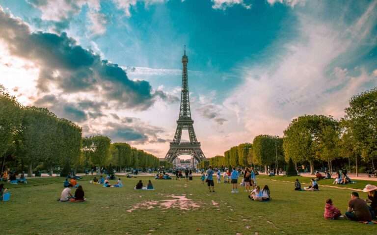 Em um final de tarde, paisagem de Torre Eiffel com pessoas e árvores ao redor, ponto turístico com diversas curiosidades sobre a França