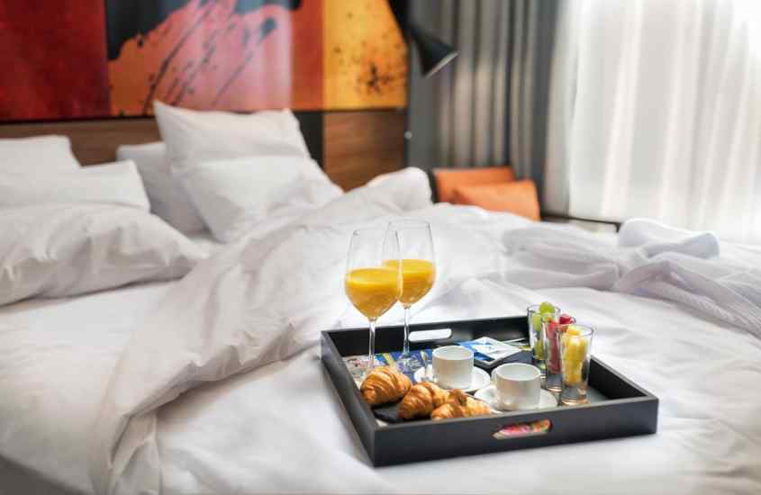 Quarto de hotel com cama de casal, bandeja de café da manhã, quadro decorativo, poltrona e luminária