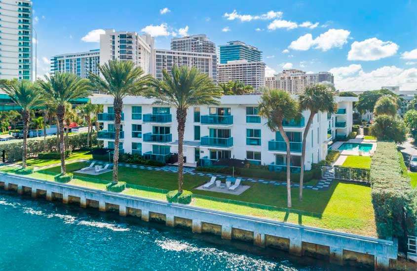 Em um dia de sol, parte de trás de um dos melhores hotéis em Miami Beach com árvores, parte gramada, piscina, espreguiçadeiras e mar na frente