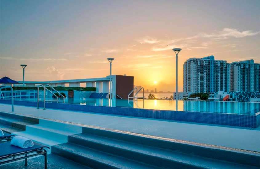 Durante o pôr do sol, área de lazer de um dos melhores hotéis em Miami Beach com piscina de borda infinita, espreguiçadeiras e cidade na frente