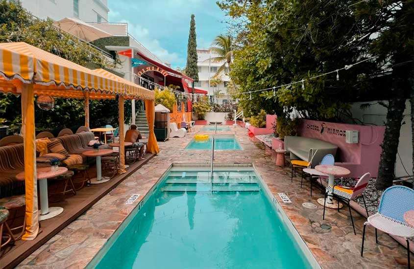 Durante a tarde, área de lazer de um dos melhores hotéis em Miami Beach com piscinas, sofás, mesas, cadeiras e árvores ao redor