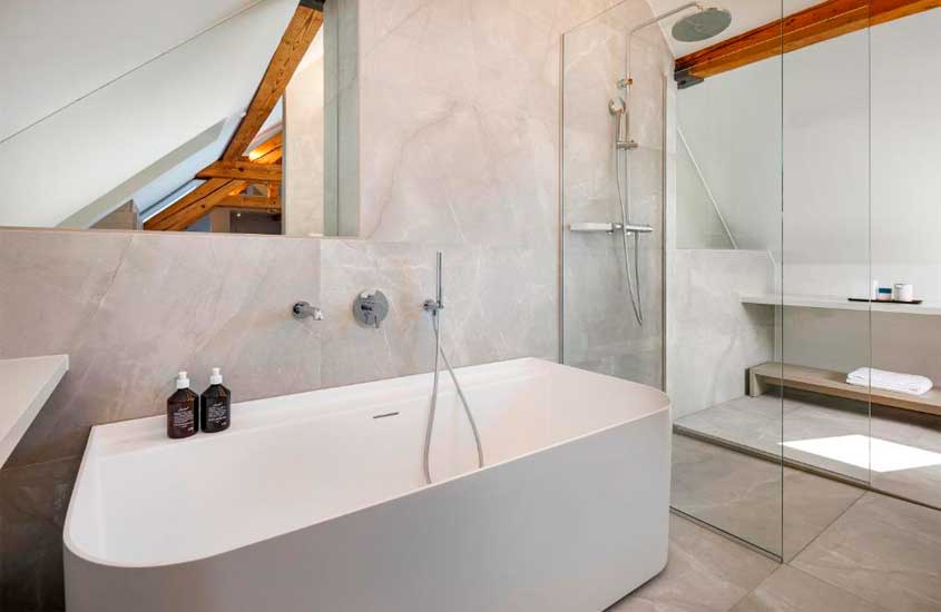 Banheiro de um hotel com banheira, box, espelho, toalhas e produtos de higiene
