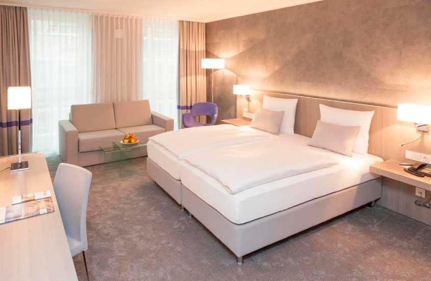 Quarto de um dos hotéis perto da Oktoberfest Munique com cama de casal, sofá, janela acortinada, mesa de trabalho e luminárias decorativas