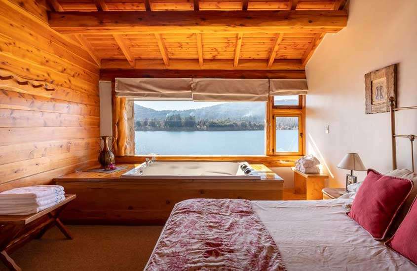 Quarto de um hotel em bariloche com cama de casal, banheira, toalhas, quadro decorativo e janela com paisagem do mar e das montanhas