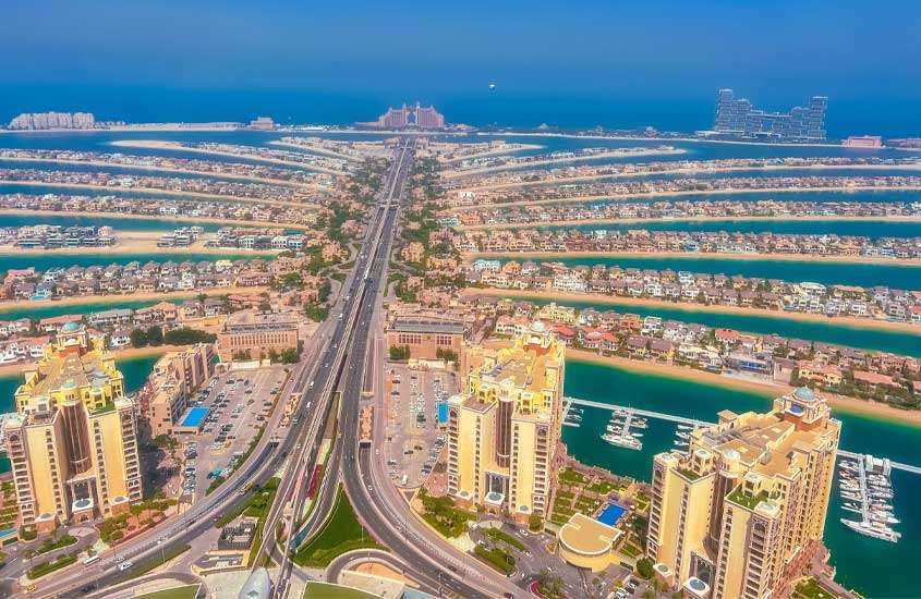 Em um dia de sol, vista aérea de um dos lugares em Dubai mais famosos com prédios, canais, barcos, carros e árvores