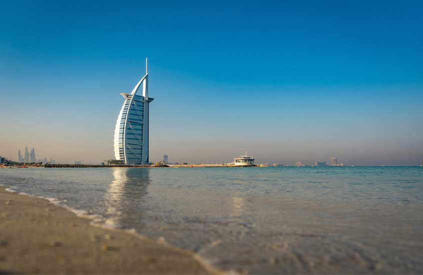 Durante uma manhã ensolarada, paisagem de um dos lugares em Dubai com praia na frente e arranha-céu atrás