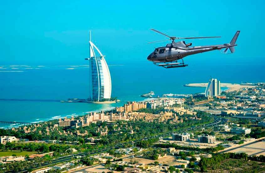 Em uma manhã de sol, vista aérea da cidade de Dubai com helicóptero sobrevoando, árvores, prédios e arranha-céus
