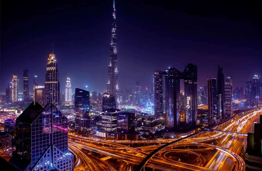 Durante a noite, vista aérea de um dos lugares em Dubai com prédios altos e ruas iluminadas