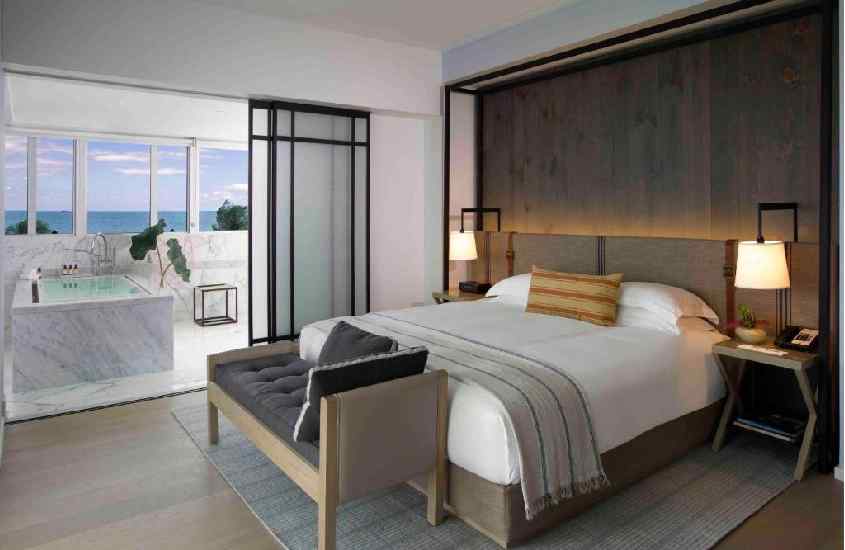 Quarto de hotel em Miami Beach com cama de casal, tapete, luminária, banheira e janela grande