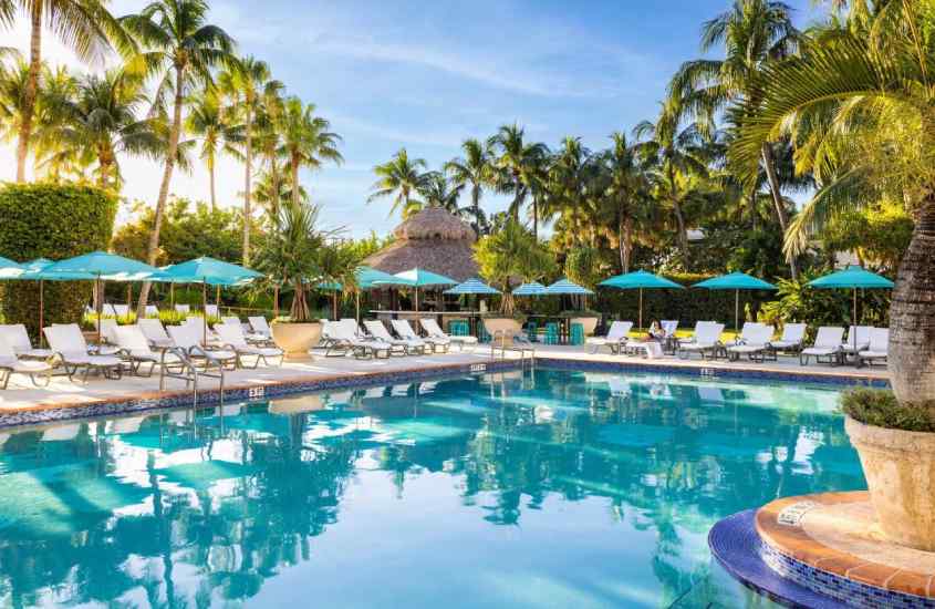 Durante o entardecer, área de lazer de hotel em Miami Beach com piscina, espreguiçadeiras, guarda-sóis, árvores e plantas ao redor