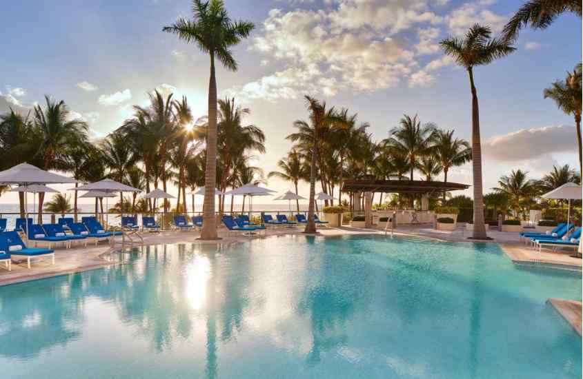 Durante o pôr do sol, área de lazer de hotel em Miami Beach em frente à praia com piscina, espreguiçadeiras, guarda-sóis, árvores ao redor e praia no fundo